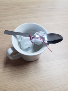 Teebeutel hängt an einem Löffel über einer Tasse