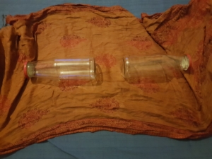 Zwei Flaschen liegen mit dem Flaschenboden zueinander in der Mitte eines Schals. Die Flaschendeckel schauen in Richtung der beiden Enden des Schals.