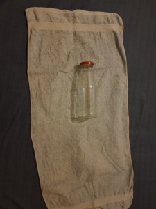 Eine Flasche liegt in der Mitte des Handtuchs, mit dem Deckel Richtung schmales Ende.