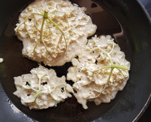 Die Blüten·dolden backen im Teig in der Pfanne aus.