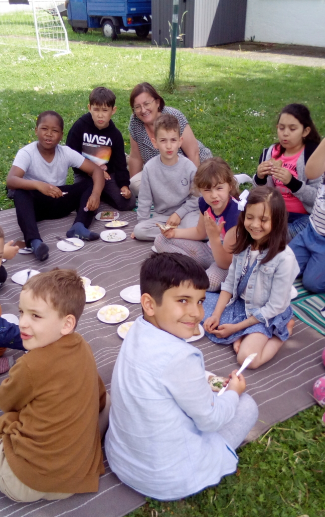 Foto der Kinder mit ihrer Lehrerin beim Picknick auf unserer Wiese. Sie essen gerade Brote mit Butter und Kräutern. (Foto: Katharina Gebel)