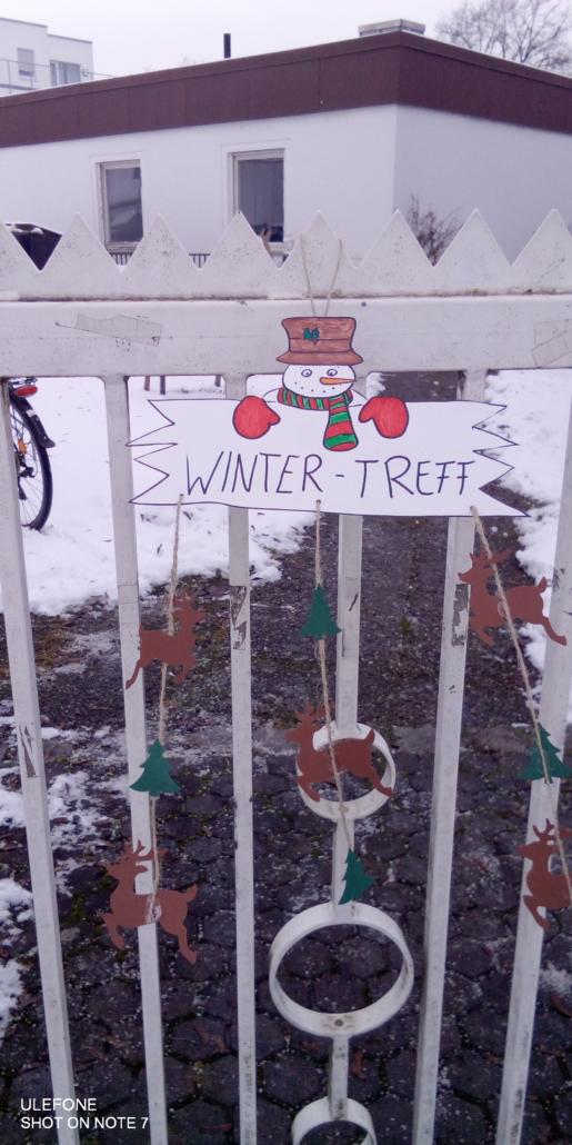 Foto des Eingangstors zum Inklusiven Garten. Daran hängt ein Schild mit dem Schriftzug "Winter-Treff". Das Schild ist mit einem Schneemann bemalt. (Foto: Katharina Gebel)