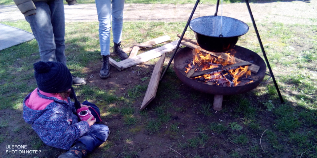 Das Foto zeigt eine Feuerschale mit einem Suppentopf. Ein Kind sitzt davor und beobachtet das Feuer. (Foto: Stadtjugendring)
