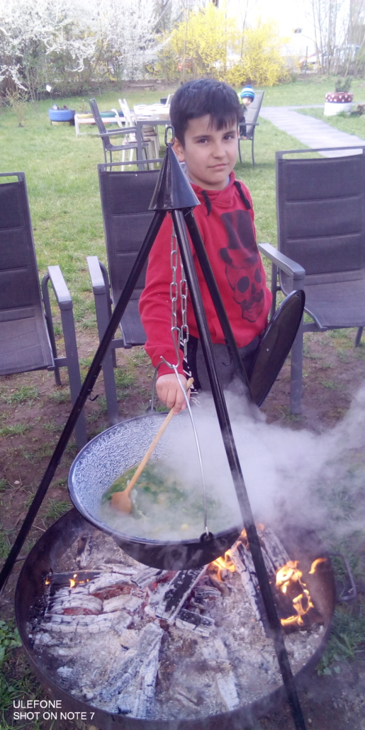Das Foto zeigt ein Kind, das die Suppe im Kessel über der Feuerschale umrührt. (Foto: Stadtjugendring)