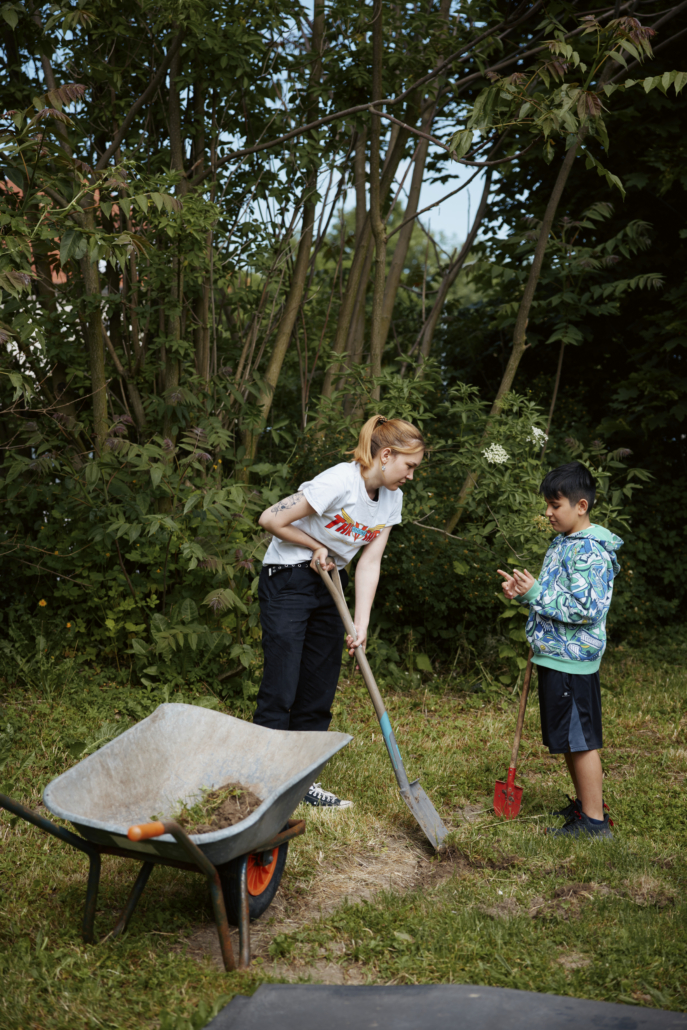Das Foto zeigt ein Kind und eine Mitarbeiterin mit Schaufeln bei der Gartenarbeit. (Foto: ©BJR/Johnke)