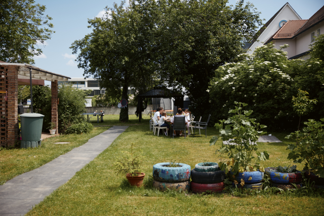 Das Foto zeigt unseren Garten. In der Mitte des Fotos ist ein Tisch, an dem alle zum Mittagessen sitzen. (Foto: ©BJR/Johnke)