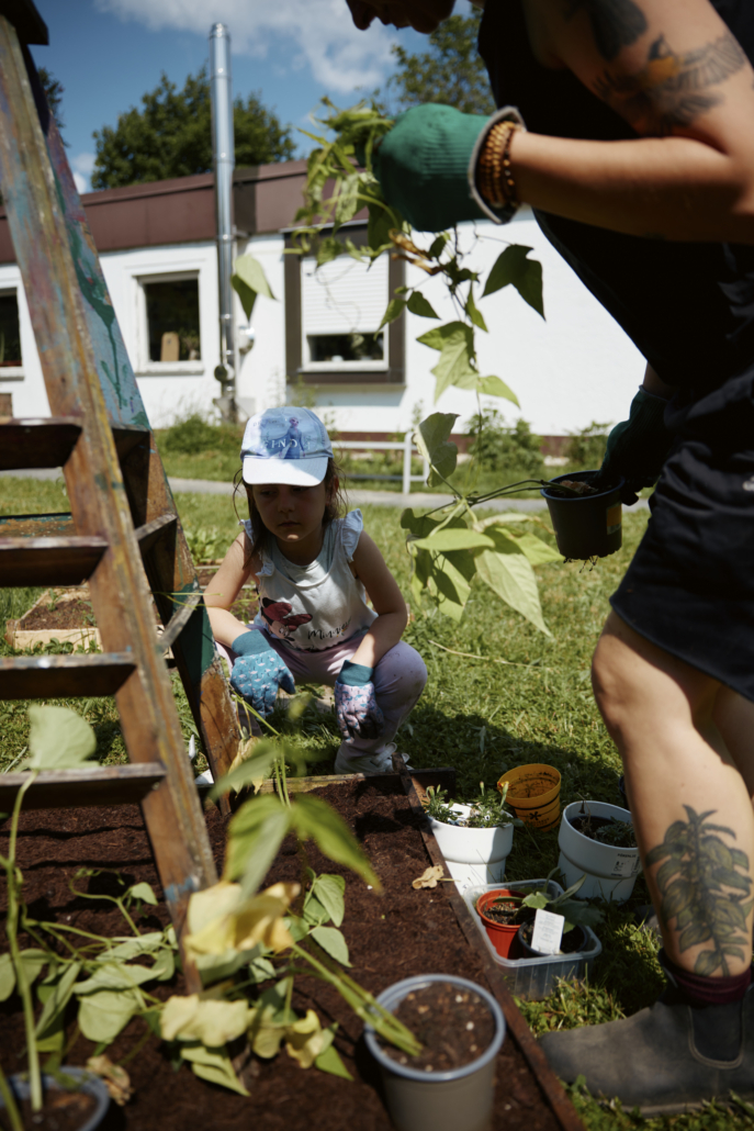 Das Foto zeigt ein Kind und die Projektleitung beim Einpflanzen von Bohnen-Ranken. (Foto: ©BJR/Johnke)