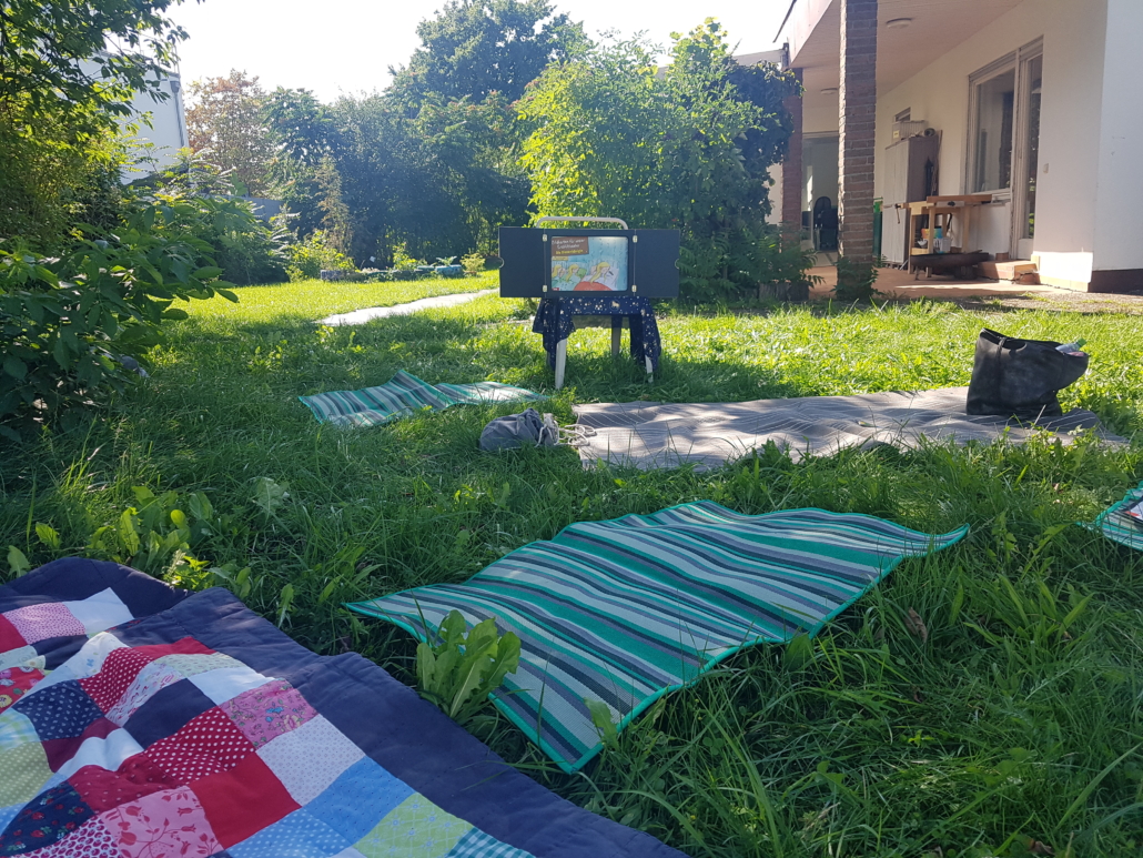 Das Foto zeigt unsere Wiese mit Decken und dem Erzähl-Theater Kamishibai auf einem Stuhl. (Foto: Irina Rakos)